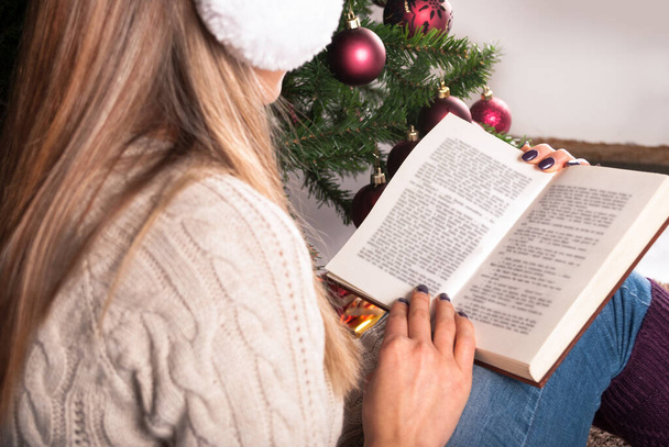 Giovane ragazza che legge il libro e seduto sull'albero di Natale è sfondo, primo piano - Foto, immagini