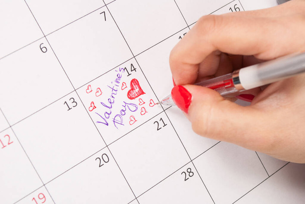 Дівчинка з олівцем малює серця і слова в календарі для Валентинів день. - Фото, зображення
