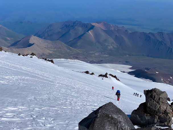 Mountain Elbrus. Climbers with backpacks and trekking poles walk along a snowy path. Beautiful mountain winter landscape. Snowy slopes of the northern Elbrus region. - Zdjęcie, obraz