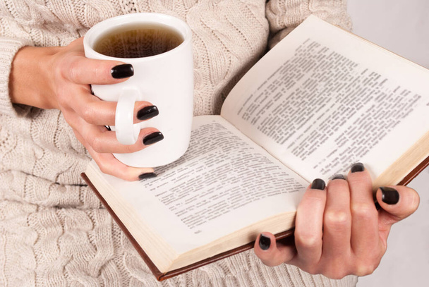 Dziewczyna trzyma książkę i filiżankę herbaty w rękach i czytania, zbliżenie - Zdjęcie, obraz