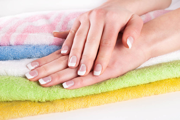 Beautiful woman hands with french nails manicure on colorful towels - Photo, Image