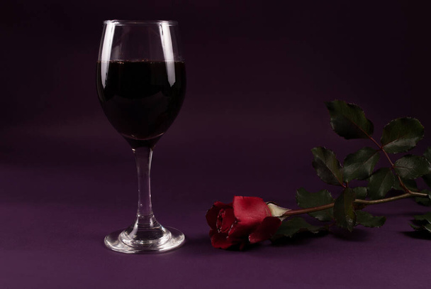 Бокал вина и красный цветок розы на темно-фиолетовом фоне, сдержанный
 - Фото, изображение