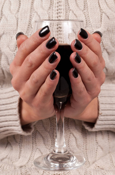 Junge weibliche Hände mit schwarzen Nägeln und Pullover, die ein Weinglas halten, aus nächster Nähe - Foto, Bild
