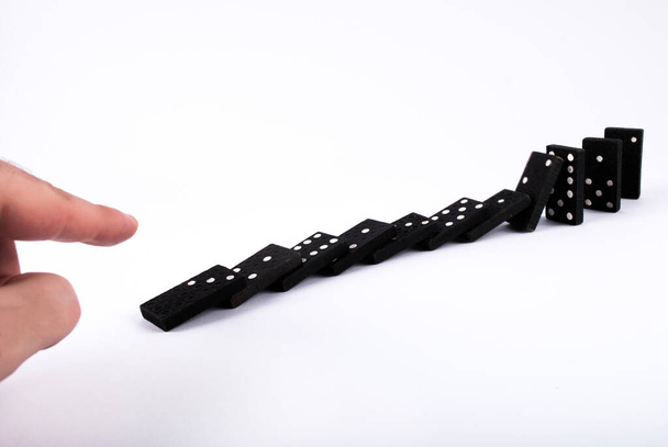 Los dedos empujan los dominós y caen aislados sobre un fondo blanco. Efecto dominó
 - Foto, Imagen