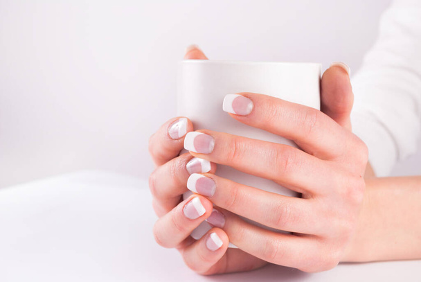 Koffiecup in jonge vrouw handen met franse nagels manicure. Sluiten. - Foto, afbeelding