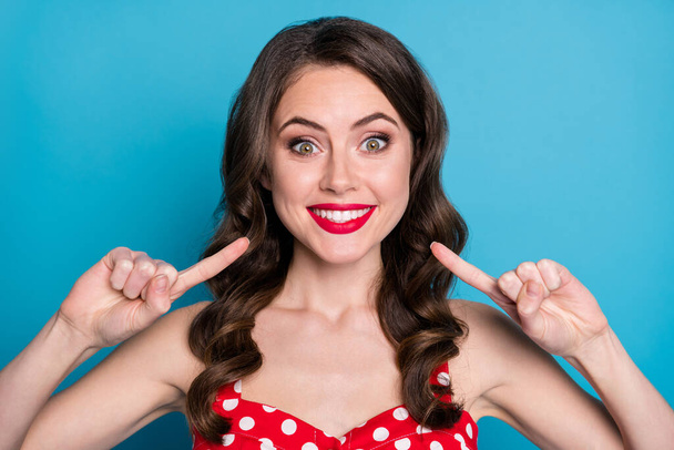 Closeup photo of pretty funny wavy lady toothy beaming smile directing finger mouth white bleaching teeth whitening procedure wear red dotted dress singlet isolated blue color background - Fotó, kép