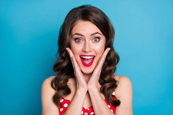 Closeup photo of pretty funny shocked wavy lady arms on cheeks open mouth excited listen good news overjoyed expression wear red dotted dress singlet isolated blue color background - Fotó, kép
