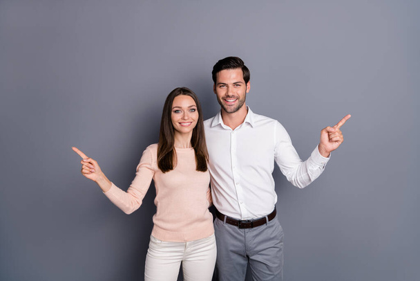 Photo beautiful lady handsome guy couple sale managers good mood direct fingers side empty space showing novelty low price shopping product wear shirts pants isolated grey color background - Valokuva, kuva
