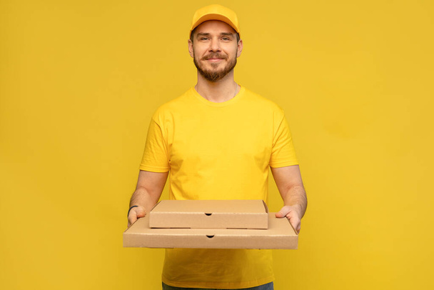 Portrait of young delivery man in yellow uniform with pizza boxes isolated over yellow background. - Foto, Imagen