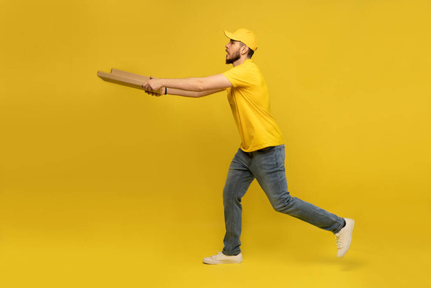Portrait of young delivery man in yellow uniform with pizza boxes isolated over yellow background. - Photo, image