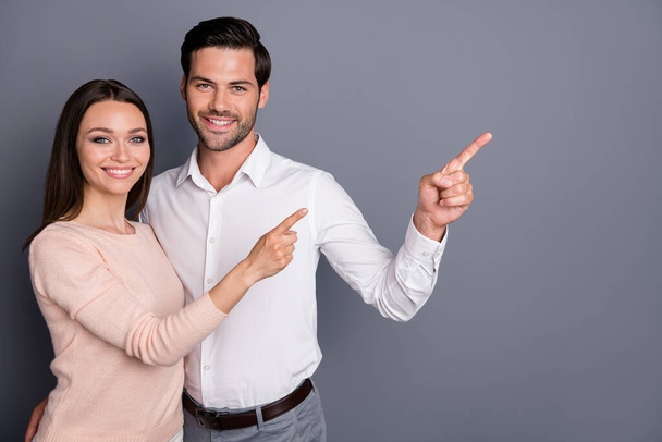Photo beautiful lady handsome guy couple sale managers good mood direct fingers side empty space showing novelty low price shopping product wear shirts isolated grey color background - Photo, Image