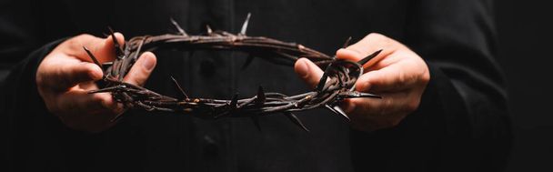 horizontal crop of priest holding wreath with spikes isolated on black  - Photo, Image