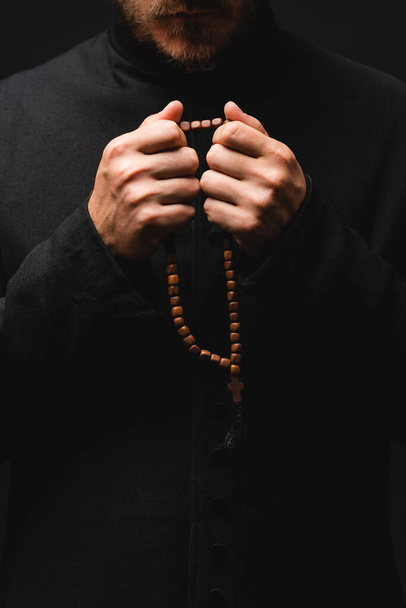 cropped view of priest holding rosary beads in hands isolated on black  - 写真・画像