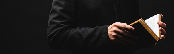 ιστοσελίδα κεφαλίδα του ιερέα κρατώντας Αγία Γραφή σε χέρια που απομονώνονται σε μαύρο  - Φωτογραφία, εικόνα