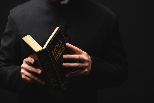 partial view of pastor holding holy bible in hands isolated on black  - Photo, Image