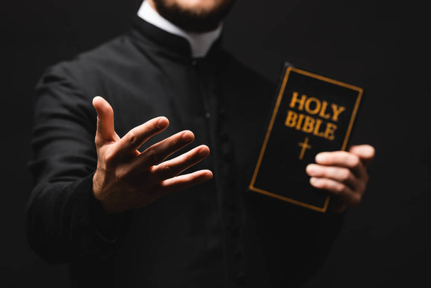 foco seletivo de pastor segurando bíblia sagrada enquanto gesticulando isolado em preto
  - Foto, Imagem
