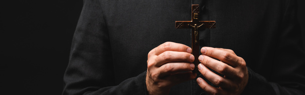panoramic crop of pastor holding wooden cross isolated on black  - Zdjęcie, obraz