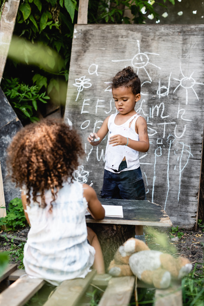 selective focus of poor african american kid standing near chalkboard and curly boy  - Fotó, kép
