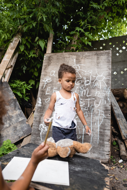 wybiórcze skupienie biednego afrykańskiego chłopca stojącego w pobliżu tablicy i dziecka - Zdjęcie, obraz