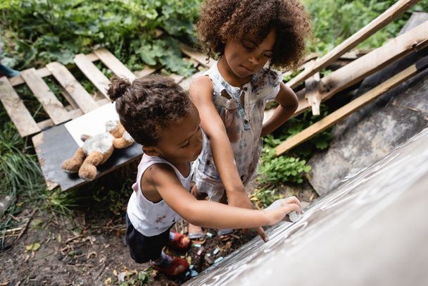 Overhead-Ansicht armer afrikanisch-amerikanischer Kinder, die draußen auf Kreidetafel schreiben  - Foto, Bild