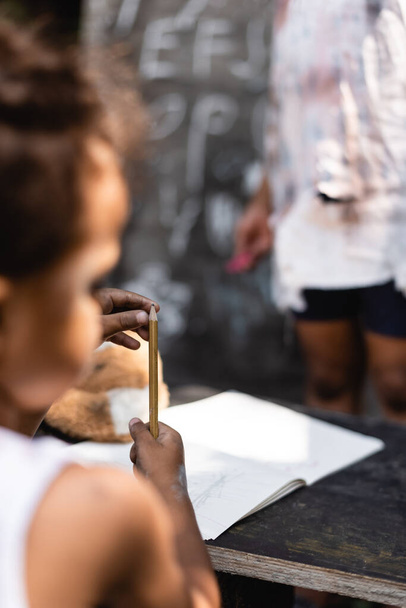 selective focus of poor african american boy holding pencil near sister - Фото, зображення