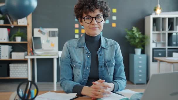 Portrait of beautiful woman looking at camera sitting at desk in creative office - Filmmaterial, Video