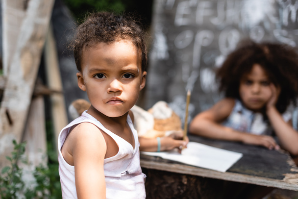 вибірковий фокус бідного афроамериканського хлопчика, який дивиться на камеру біля кучерявої сестри
  - Фото, зображення