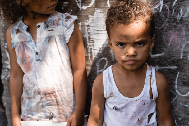 köyhä afrikkalainen amerikkalainen lapsi revitty vaatteita seisoo veljensä lähellä liitutaulu  - Valokuva, kuva