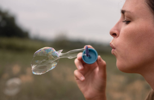 Het meisje blaast zeepbellen. Een jonge vrouw zit in de natuur en blaast zeepballen. Gezicht in profiel, zijaanzicht. - Foto, afbeelding