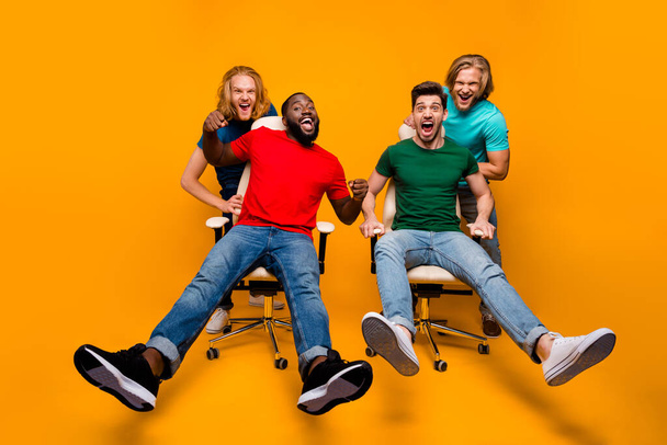 Full length photo two blonde hair men have office chair ride challenge afro american guy enjoy fun pal shout afraid fast speed wear t-shirt denim jeans isolated bright color background - Foto, Bild