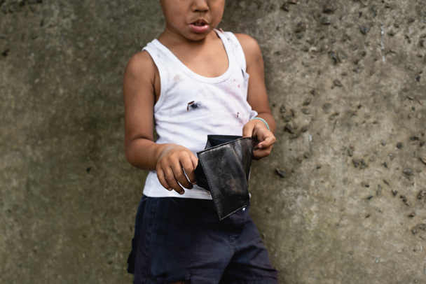 Vista recortada de un niño afroamericano pobre con ropa desordenada sosteniendo billetera en la calle urbana
  - Foto, Imagen
