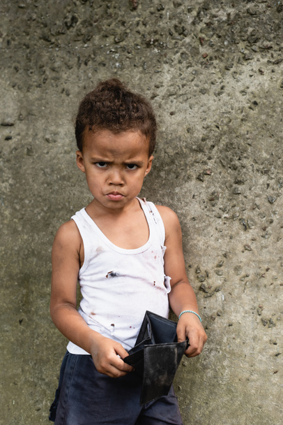 Arrabbiato afro-americano bambino in abiti disordinati in possesso di portafoglio vuoto sulla strada urbana  - Foto, immagini