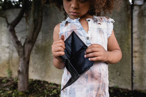 Vista recortada de un niño afroamericano pobre sosteniendo una cartera vacía en la calle urbana
  - Foto, Imagen