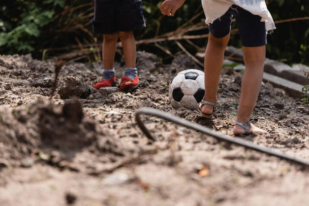 スラムの汚い道でサッカーをしている貧しいアフリカ系アメリカ人の子供たちの作物のビュー  - 写真・画像