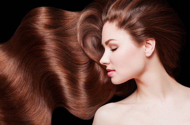 Brown Hair. Beautiful young woman with healthy luxurious long hair on dark background. Hairstyle. Hair cosmetics - 写真・画像