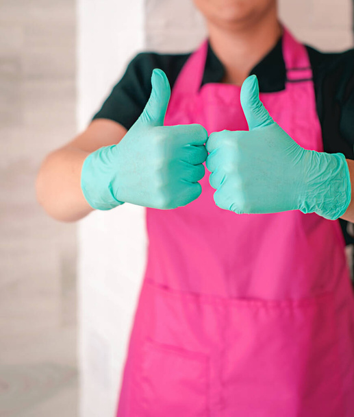 Kobieta w lateksowych rękawiczkach i różowym fartuchu trzymająca kciuki w górze jako symbol nadziei. Ok, nadzieja, wygrana koncepcja - Zdjęcie, obraz