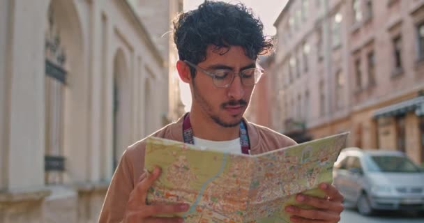Crop view of young man in glasses looking aside while walking. Handsome guy with nose ring searching address with map at old city street. Concept of travelling and tourism. - Séquence, vidéo