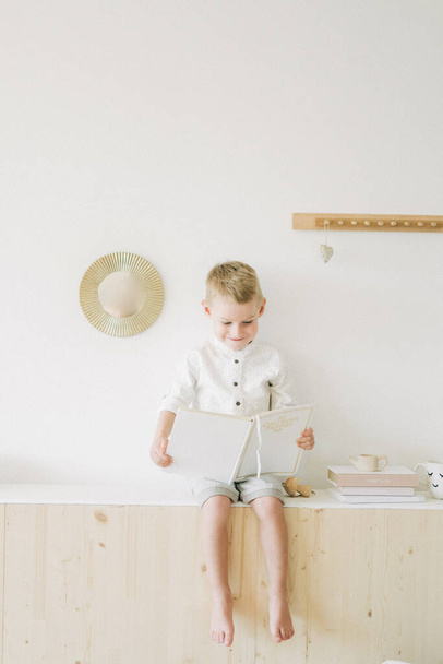 маленький мальчик играет в игрушки в белой скандинавской детской комнате дома - Фото, изображение