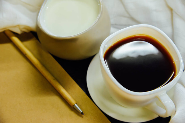 Espresso y leche en un vaso y paño blanco, cuaderno, lápiz sobre mesa de madera negra, vista superior
 - Foto, Imagen