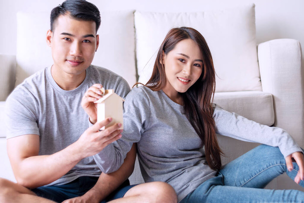 Boldogság fiatal nő üzembe pénzt érmét a faház malacka bank, míg a férje tartja metafora megtakarítás pénzt vásárolni új házat, miközben együtt ülnek a nappaliban.Tervező jövedelem koncepció. - Fotó, kép