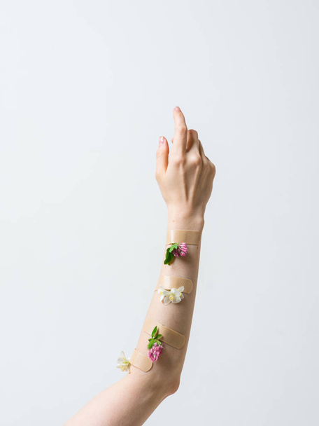 Womans hand raised up with patches and flowers isolated on white, concept photography for beauty or feminist blog. - Fotó, kép