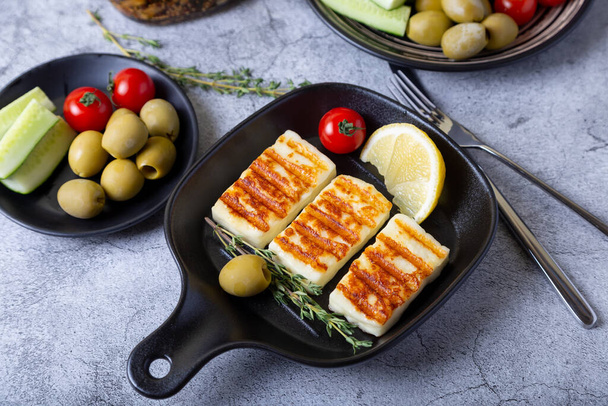 Grilled haloumi cheese on a black pan with olives, tomatoes, cucumbers and pepperoni. Close-up. - Φωτογραφία, εικόνα