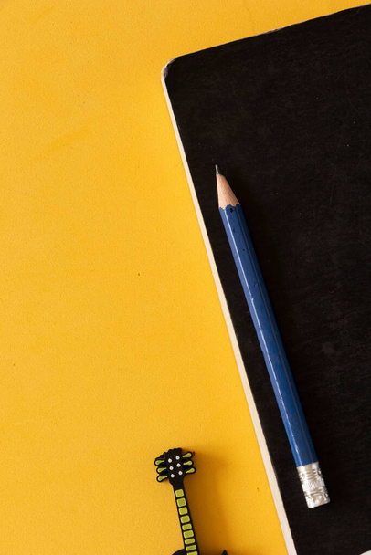Cuaderno negro con lpiz azul al lado de un disco extraíble en forma de guitarra sobre una mesa amarilla..  - Foto, Imagen