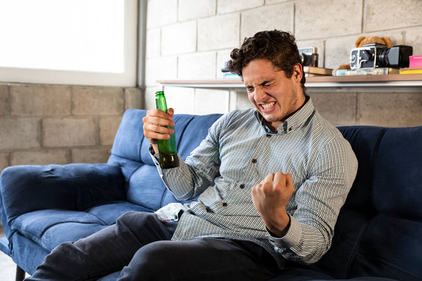 jóképű és elegáns férfi TV-t néz és sört iszik otthon a nappaliban - Fotó, kép