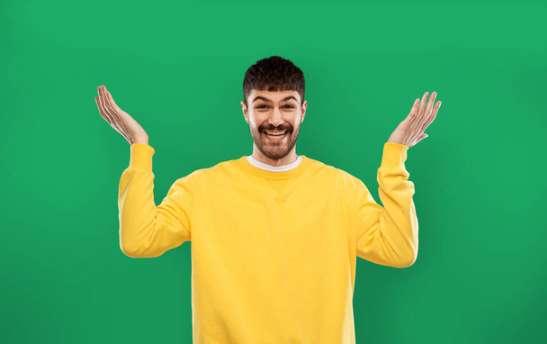 happy man in yellow sweater shrugging over green - Foto, immagini