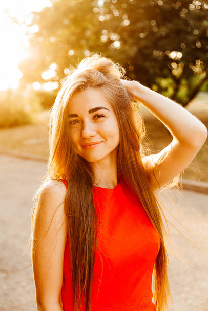 Photosession of a pretty girl walking in the city at sunset in a red dress with beautiful hair - Foto, afbeelding