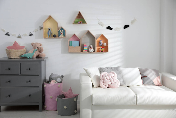 Cute children's room with house shaped shelves, sofa and chest of drawers. Interior design - Zdjęcie, obraz