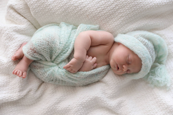 Cute newborn baby in warm hat sleeping on white plaid, top view - 写真・画像