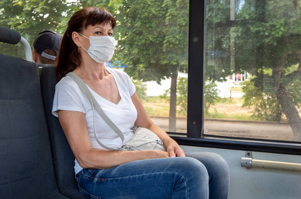 Adult woman in a protective mask rides alone in an empty on public transport in the city. Social distance. Bus passengers are protected from the coronavirus. New normal. lifestyle during the pandemic - Photo, image