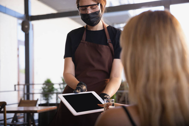 The waitress works in a restaurant in a medical mask, gloves during coronavirus pandemic - Foto, Imagem